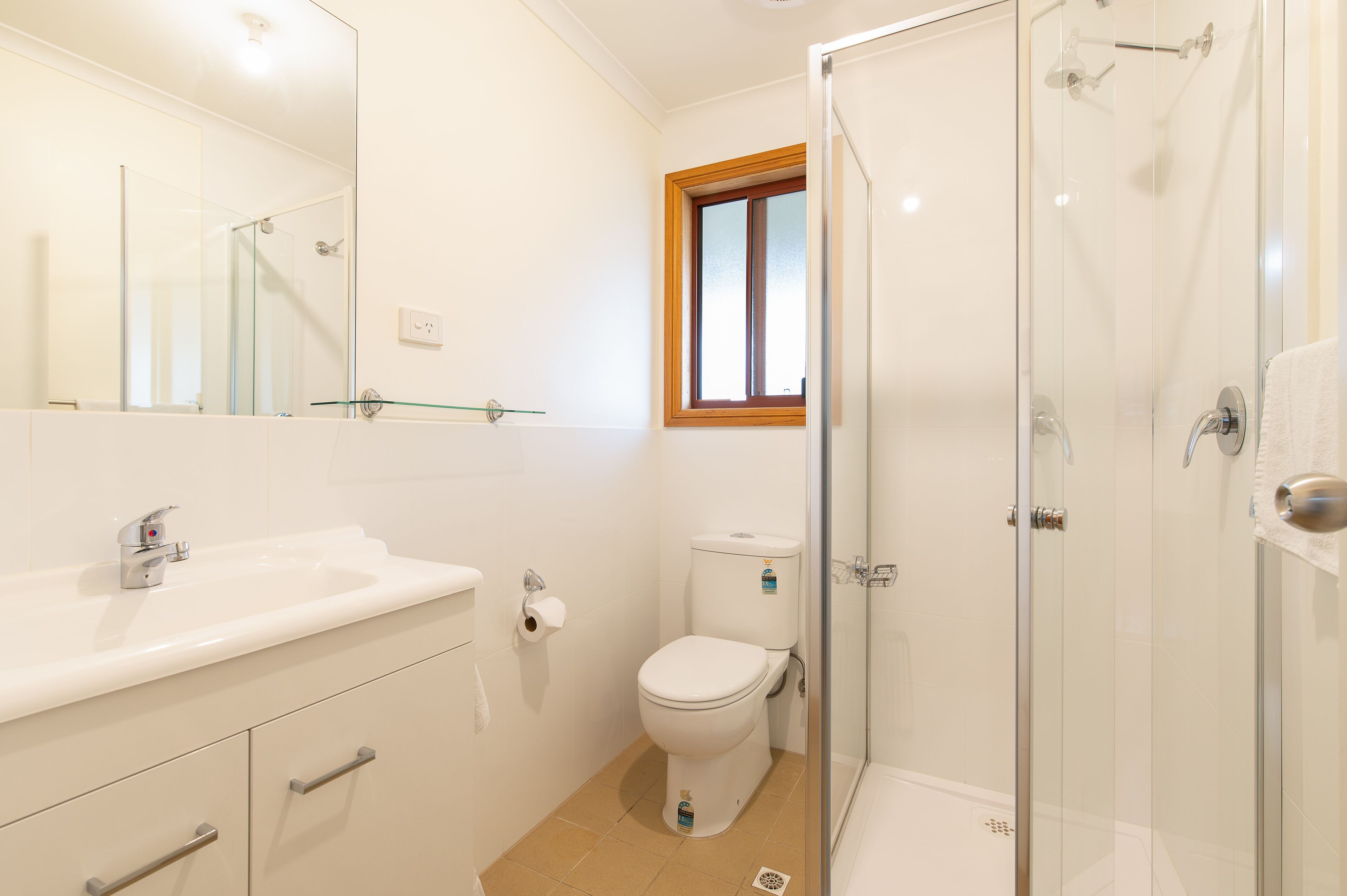 A bathroom with a glass-enclosed shower, a toilet, and a sink with a mirror above it.