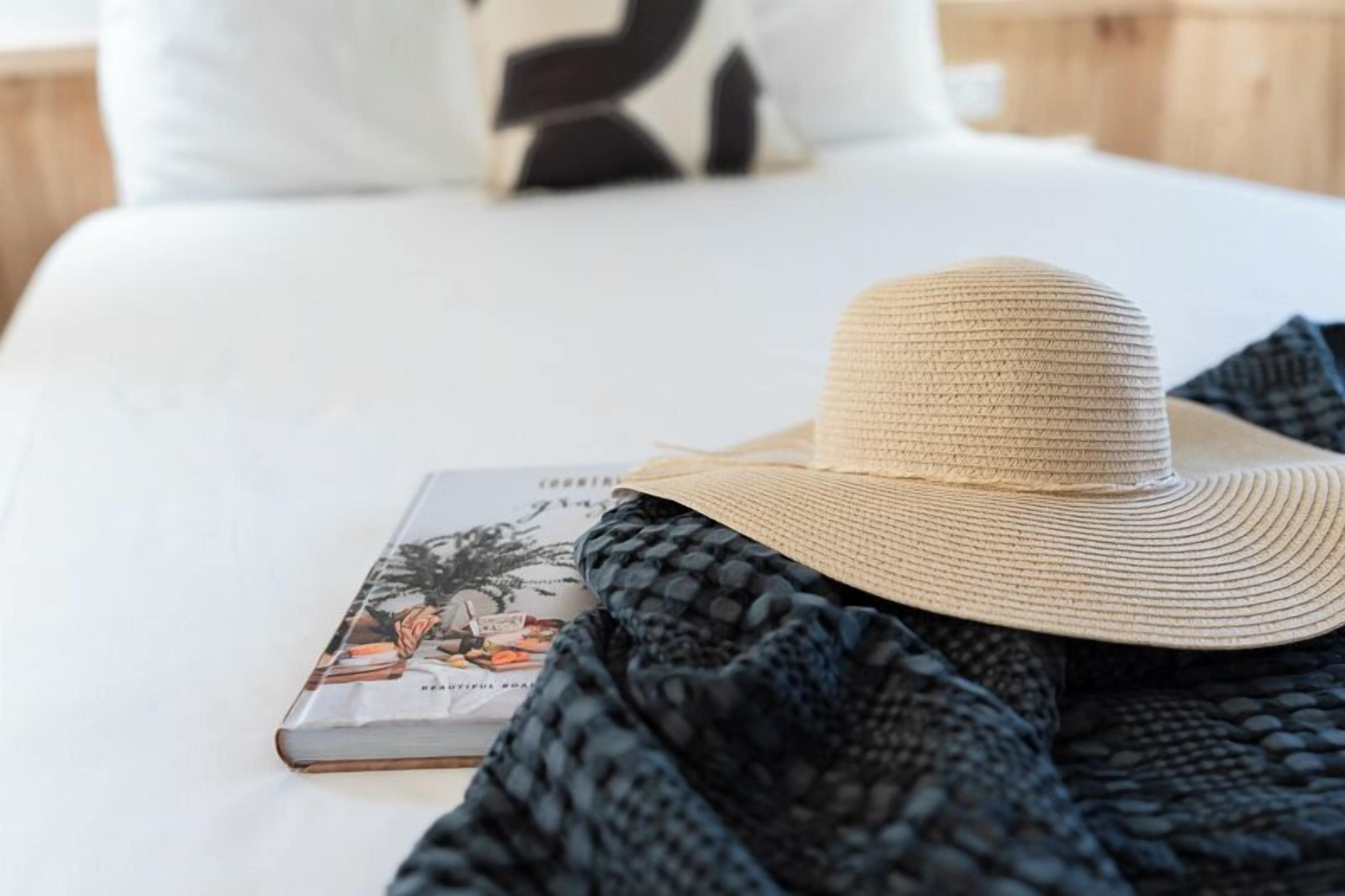 A bed with a book and a straw hat on it.