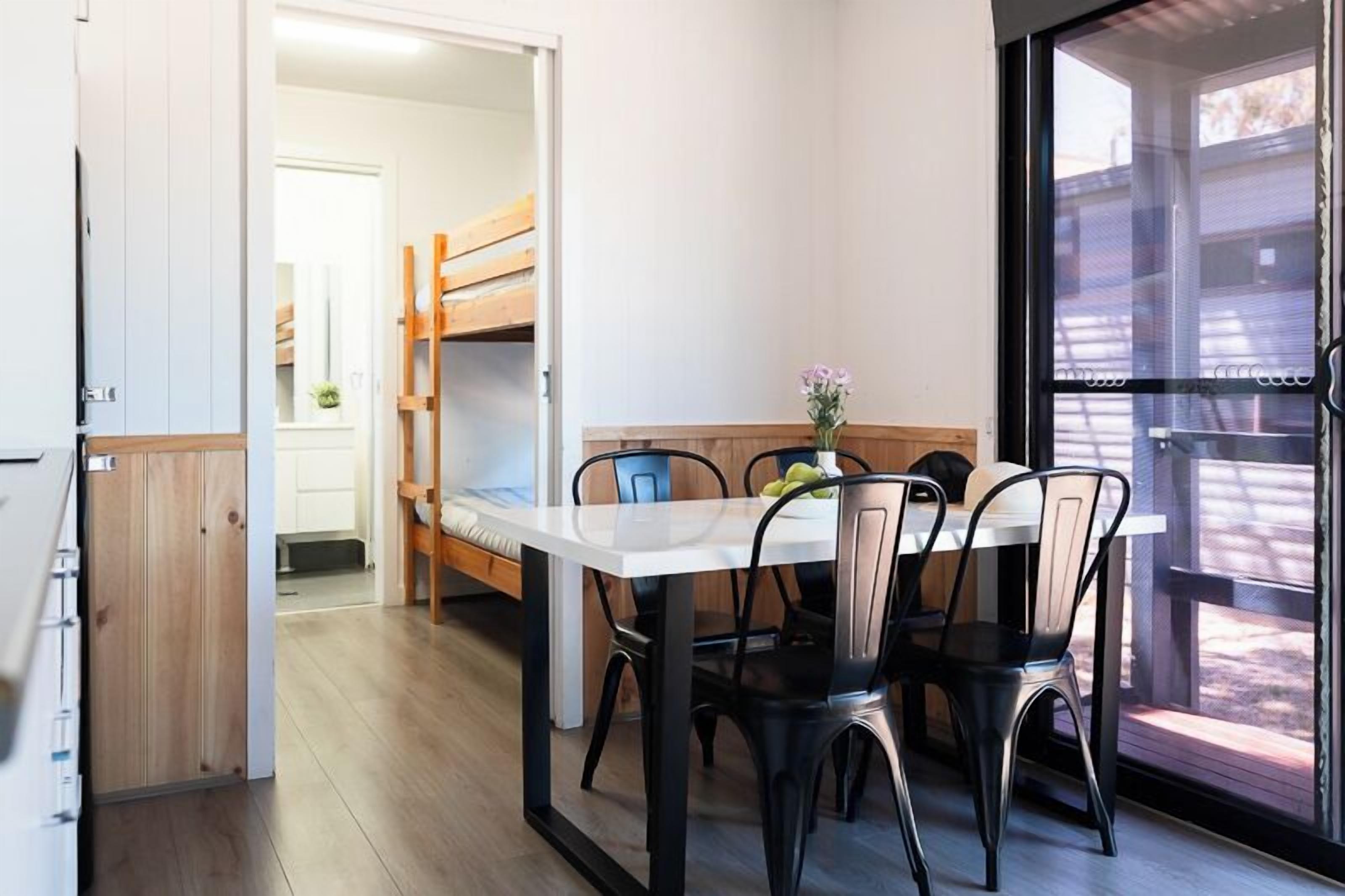 A compact kitchen with a dining area, wooden furniture, and a large window offering a view of the outside.
