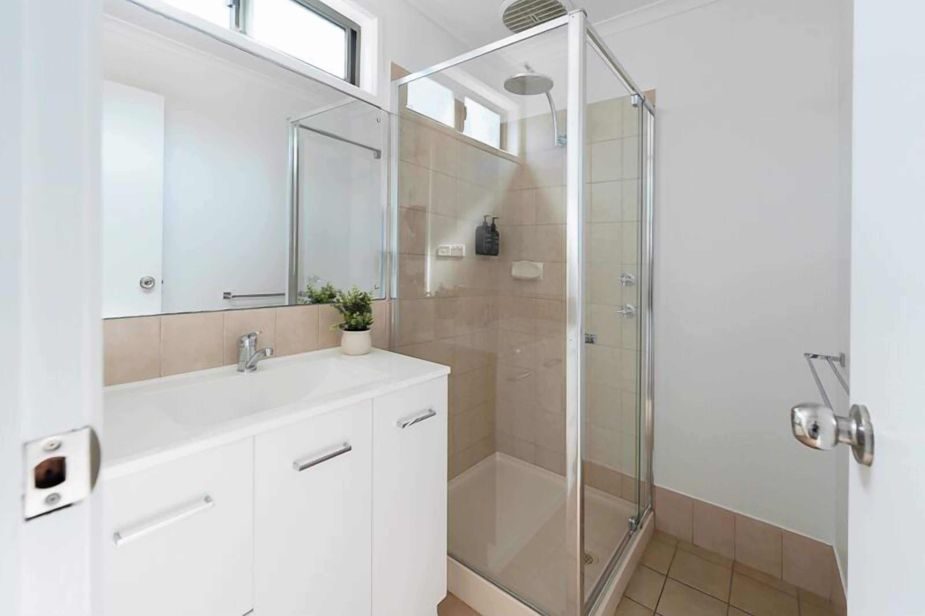 A modern bathroom with a glass shower enclosure, a white sink with a mirror, and a potted plant.