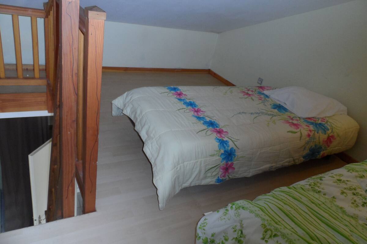 A bedroom with a bed, a wooden staircase, and a small window.