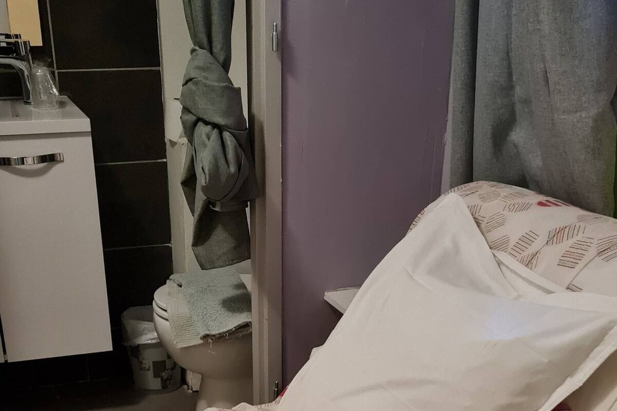 A bed with a floral-patterned bedspread, a white pillow, and a bathroom with a toilet and sink visible in the background.