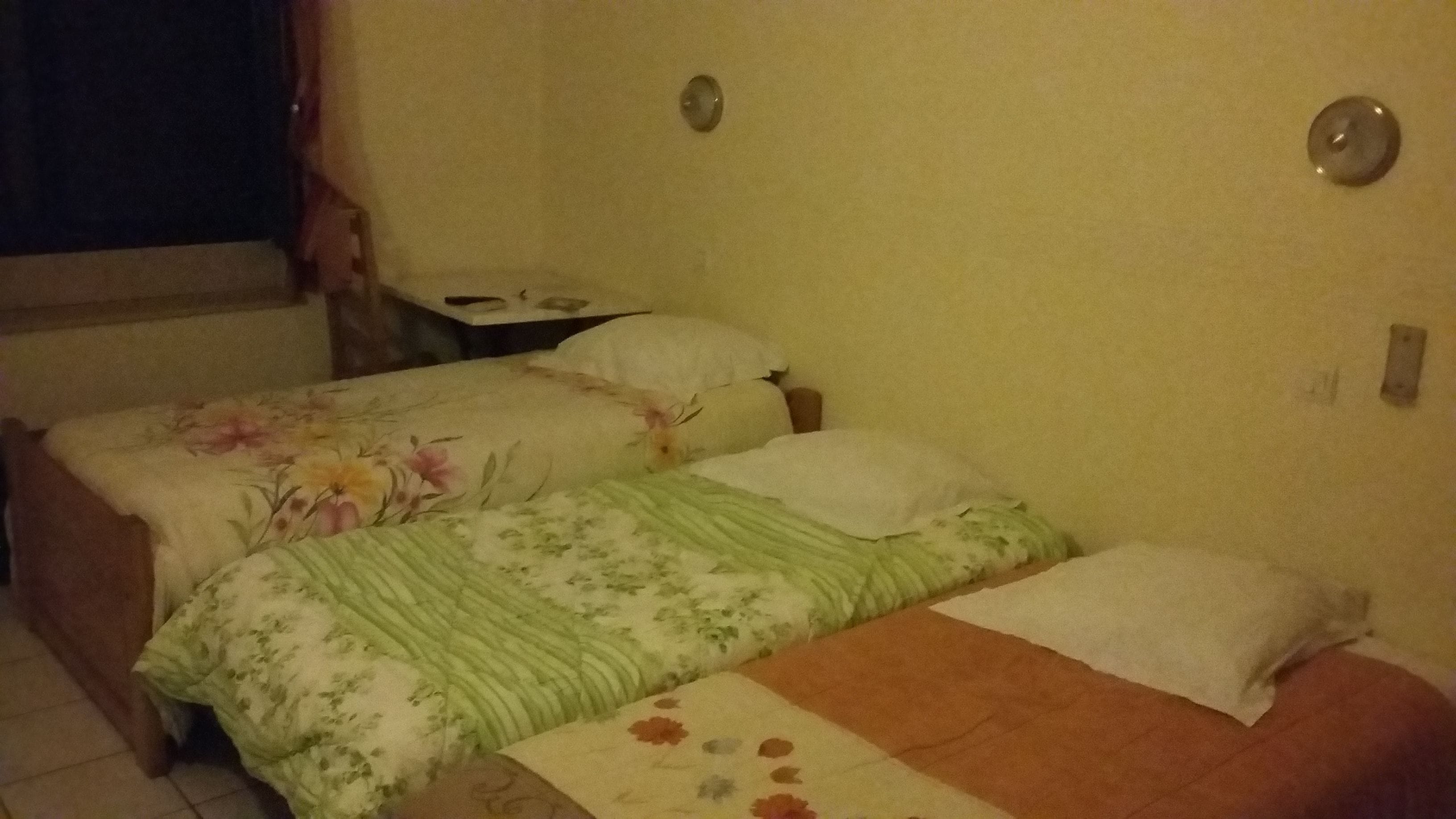 A bedroom with two beds, a nightstand, and a window with curtains.