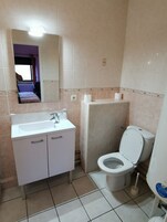 Un baño con lavamanos blanco, espejo, inodoro y una ventana pequeña.
