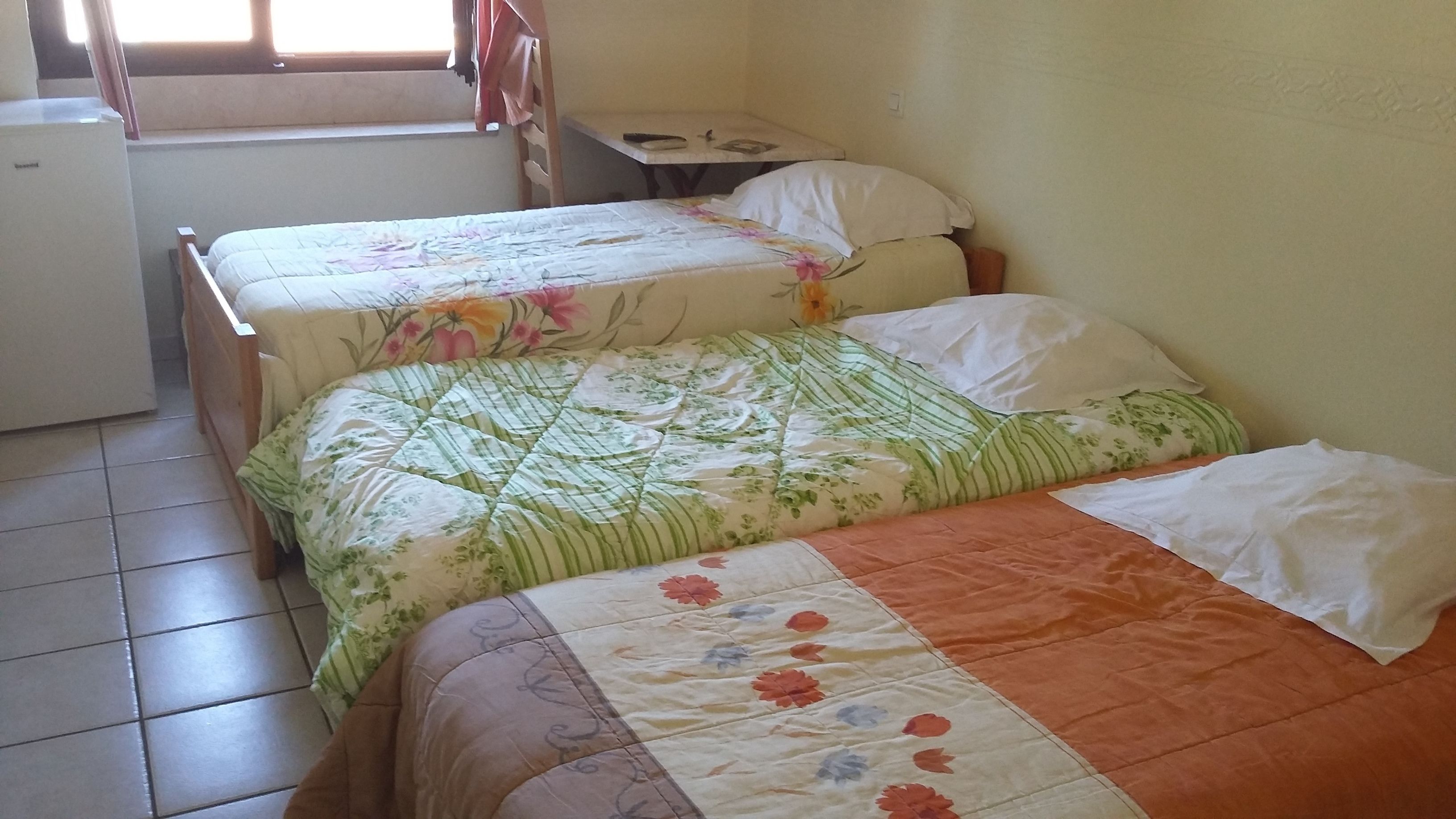Una habitación con dos camas, una mesita y un refrigerador.
