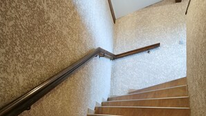 A staircase with a handrail, leading to a landing with a light switch and a wooden shelf. - Auberge de l'Europe (Saint-Quentin-Fallavier)