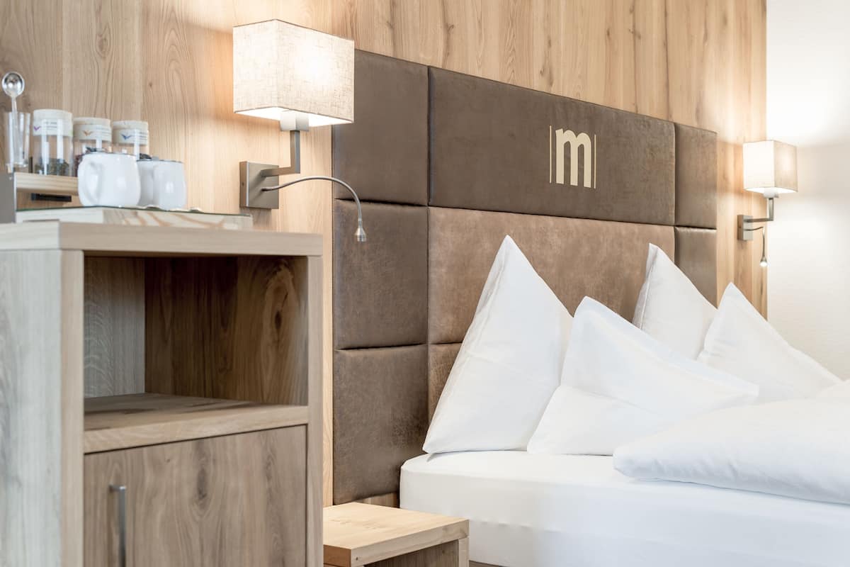 Une chambre d’hôtel moderne avec une tête de lit en bois, du linge de lit blanc et une table de chevet avec une lampe.