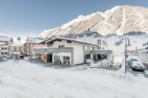 A hotel with a modern facade, a staircase leading to the entrance, and a view of snow-covered mountains in the background. - Hotel Mondin (Ischgl)