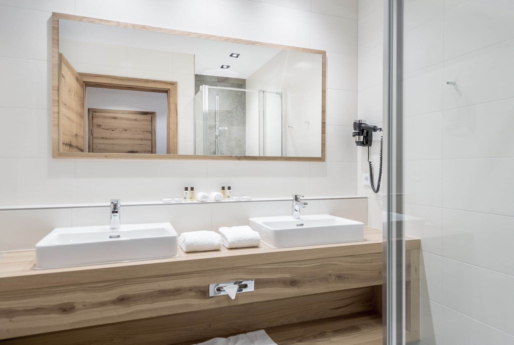 A modern bathroom with two sinks, a wooden vanity, a large mirror, and a glass shower enclosure.
