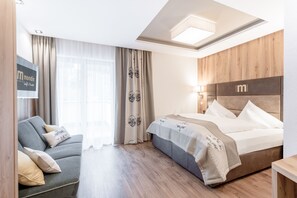 A modern hotel room with a bed, a sofa, and a wooden headboard. - Hotel Mondin (Ischgl)