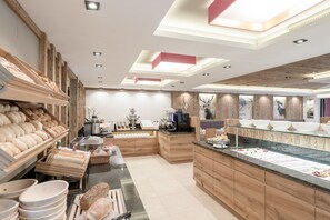 A bakery with wooden shelves of bread, a display counter with pastries, and a coffee machine. - Hotel Mondin (Ischgl)