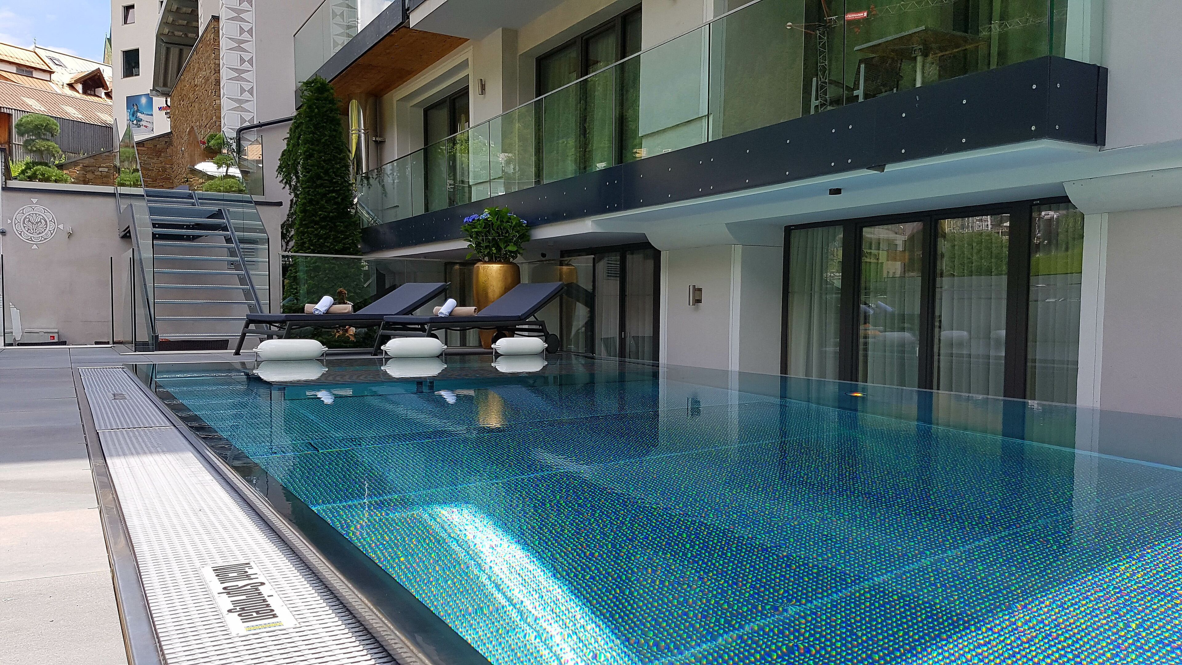 A modern swimming pool with lounge chairs and a staircase leading to an upper level.
