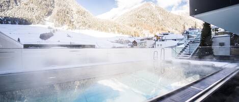 Un jacuzzi con vistas a montañas nevadas y un edificio al fondo.