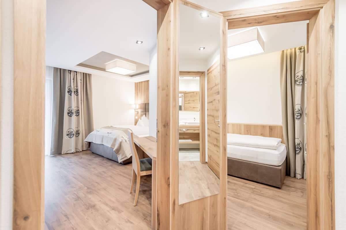Une chambre d’hôtel moderne avec un plancher en bois, un lit, un bureau et une salle de bain visible à travers une porte ouverte.