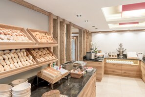 Una vitrina de panadería con panes y pasteles variados, una estación de café y un trofeo decorativo.