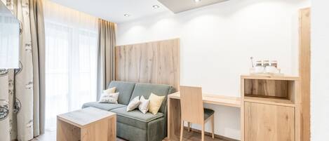 A modern living room with a grey sofa, wooden coffee table, and a wooden desk with a chair.