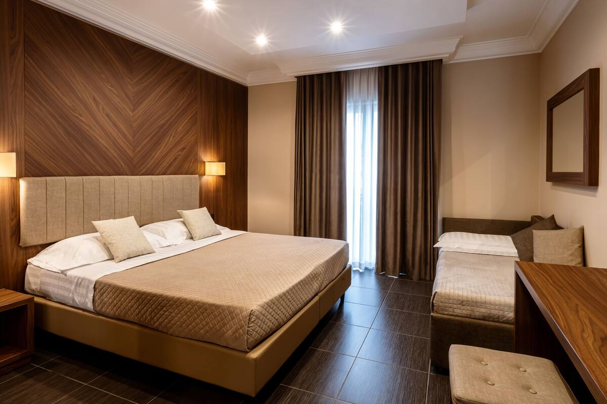 A hotel room with a large bed, a smaller bed, a desk, and a chair.