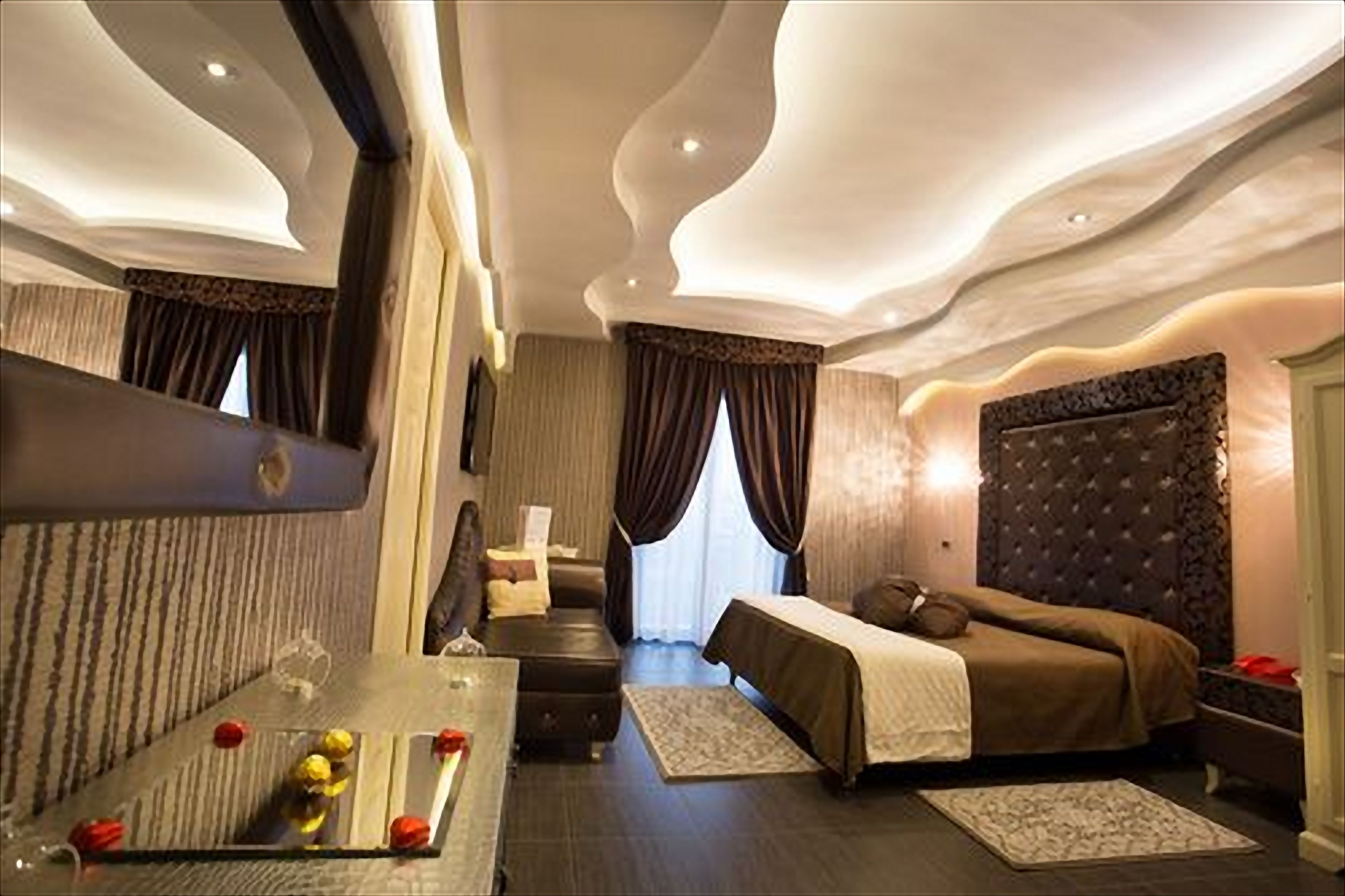 Una habitación de hotel moderna con una cama grande, una zona de estar con una mesita de cristal y un espejo amplio.