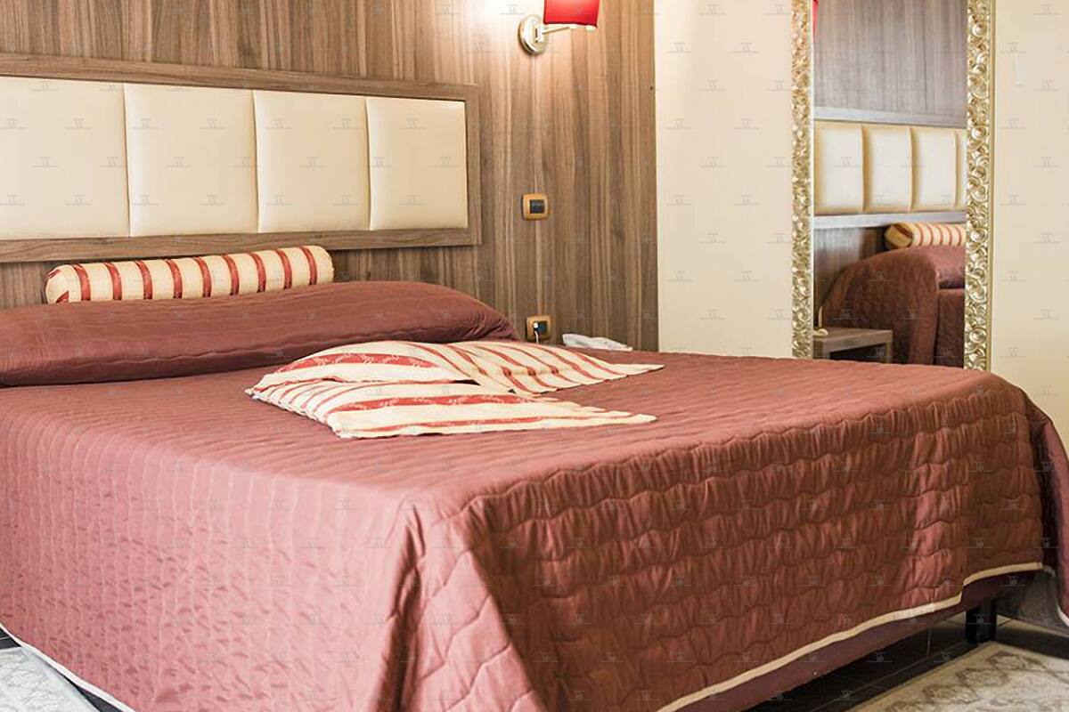 A bed with a red quilt and striped pillow, a wooden headboard, and a mirror with a gold frame.