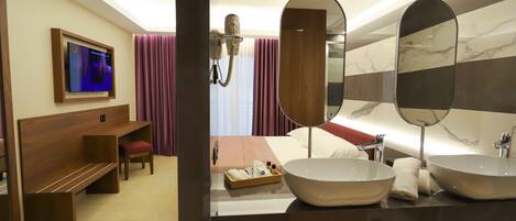 A modern hotel bathroom with two large sinks, a vanity mirror, a hairdryer, and a television mounted on the wall.
