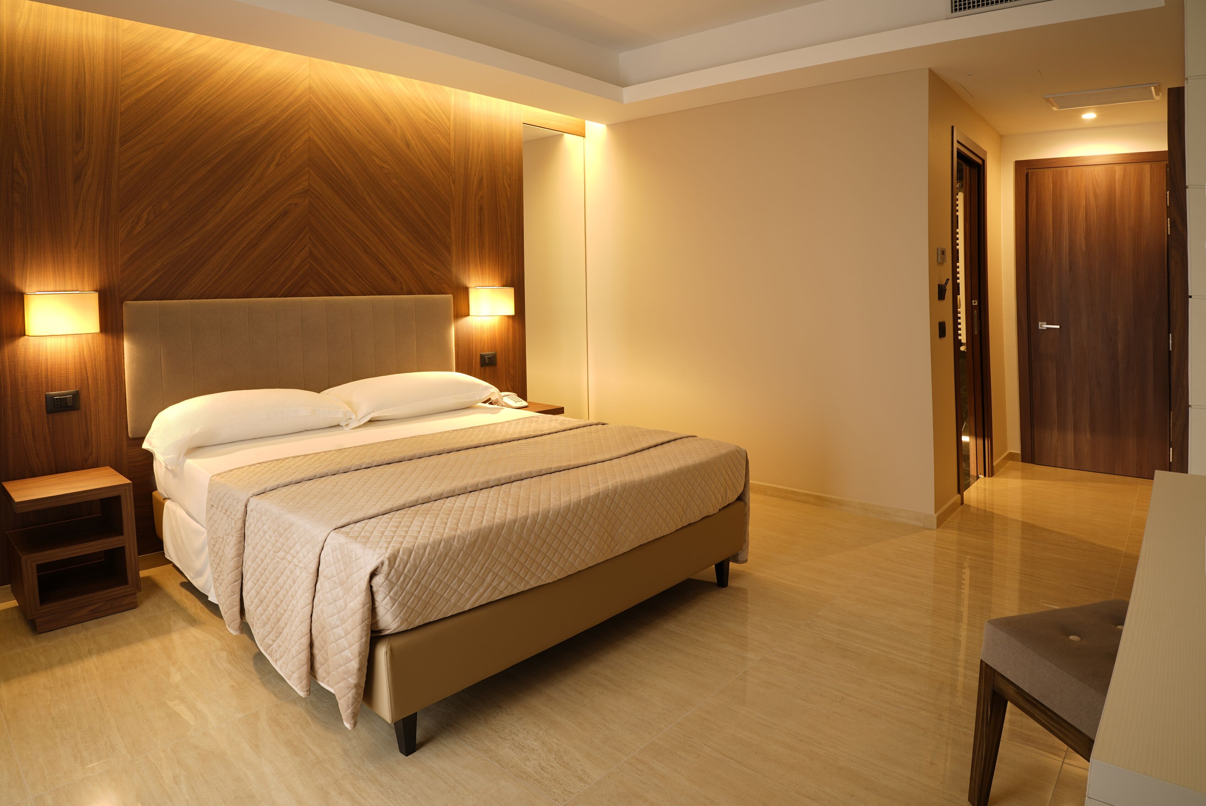Una habitación de hotel moderna con una cama grande, paneles de madera en las paredes y una puerta de madera.