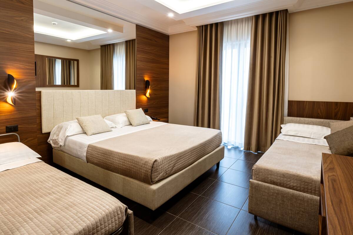 A hotel room with a large bed, two smaller beds, a sofa, and a wooden headboard.
