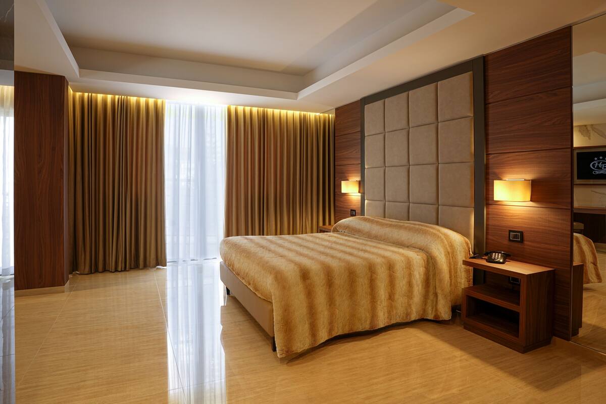 A modern hotel room with a large bed, wooden paneling, and a nightstand with a lamp.