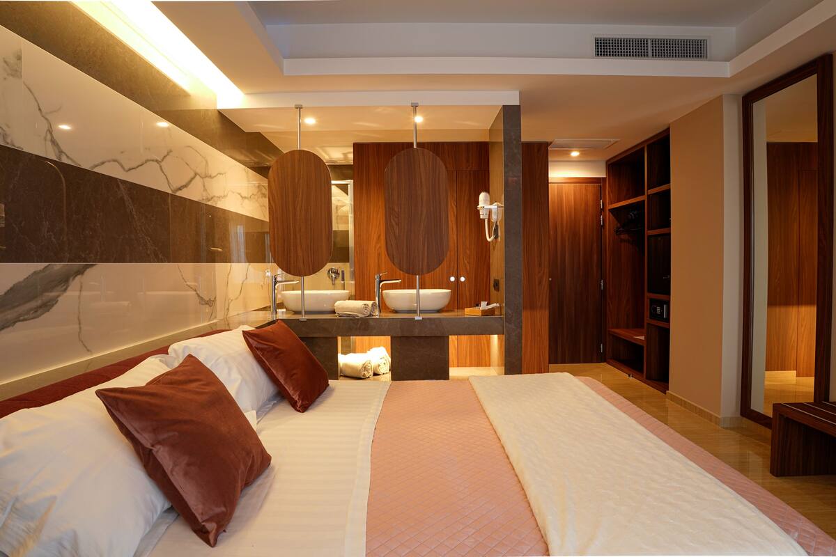 A modern hotel room with a large bed, a bathroom with a vanity, and a walk-in closet.