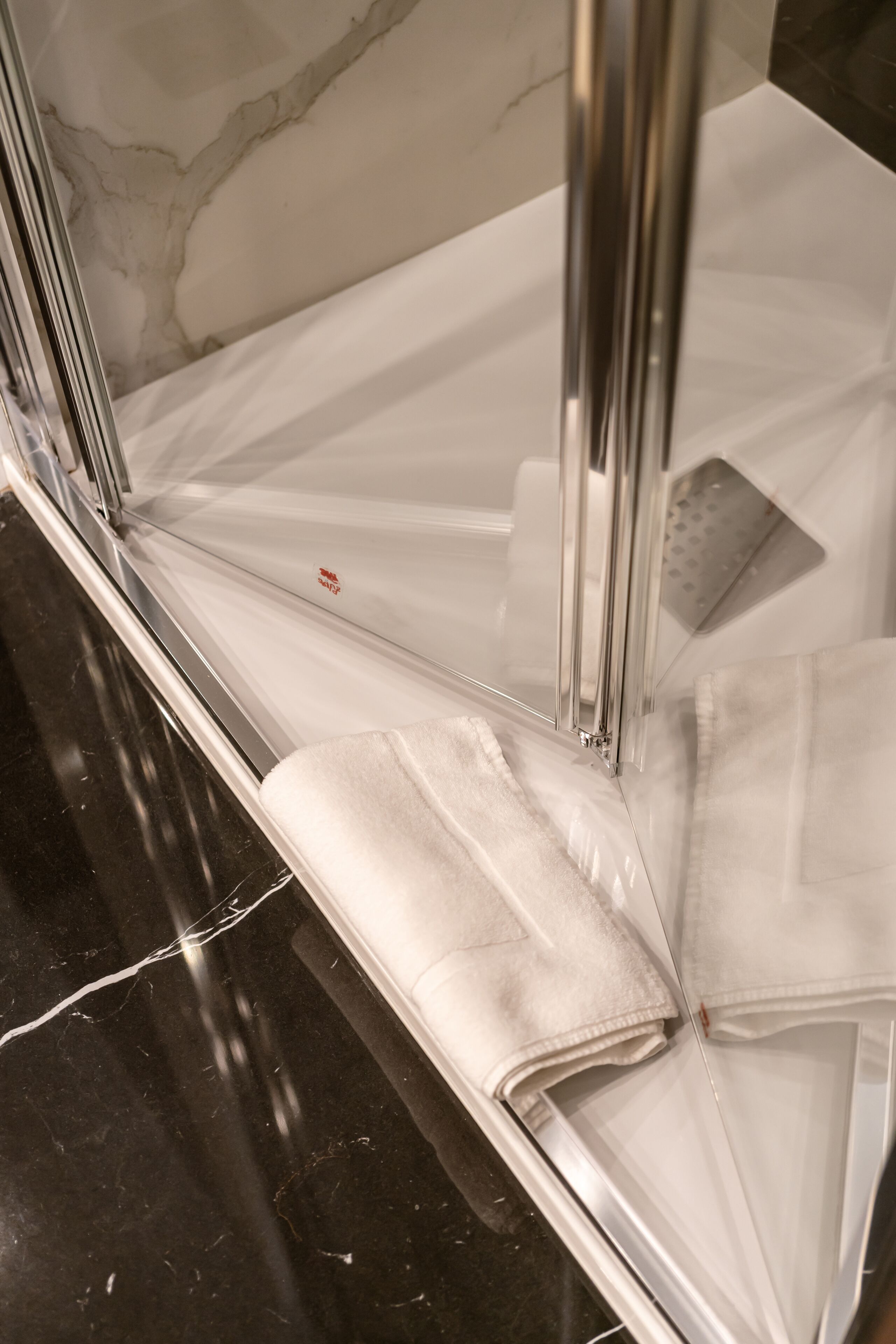 A bathroom with a white marble wall, a chrome bathtub, and a white towel.