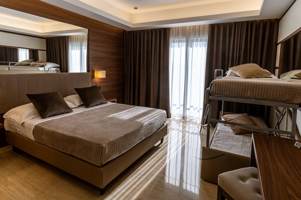 A modern hotel room with a large bed, a desk, and a bunk bed.