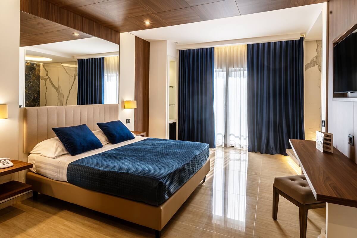 A modern hotel room with a large bed, a wooden desk, and a large mirror.