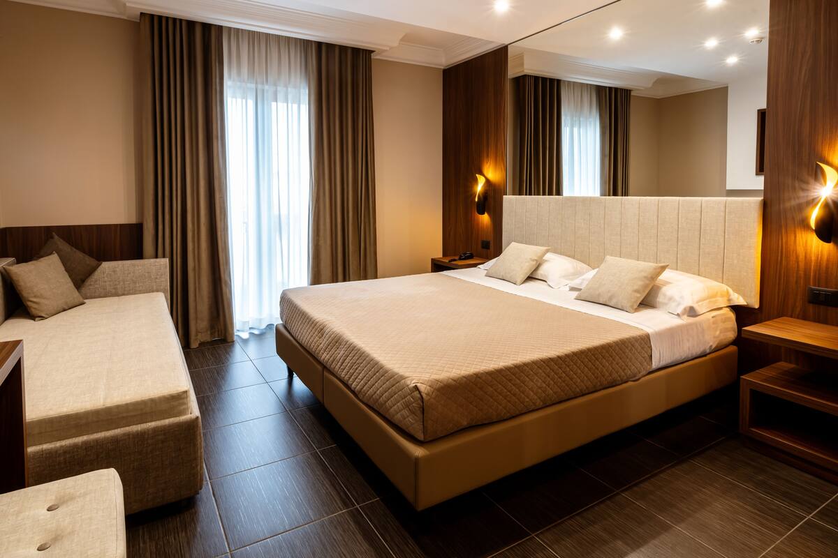 A hotel room with a large bed, a sofa, a bedside table, and a mirror.