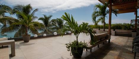 A rooftop terrace with palm trees, a pool, and a wooden pergola.