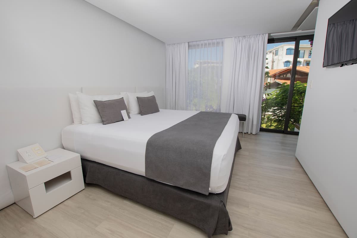 Une chambre d’hôtel moderne, dotée d’un grand lit, d’une table de chevet et offrant une vue sur l’extérieur grâce à une grande fenêtre.