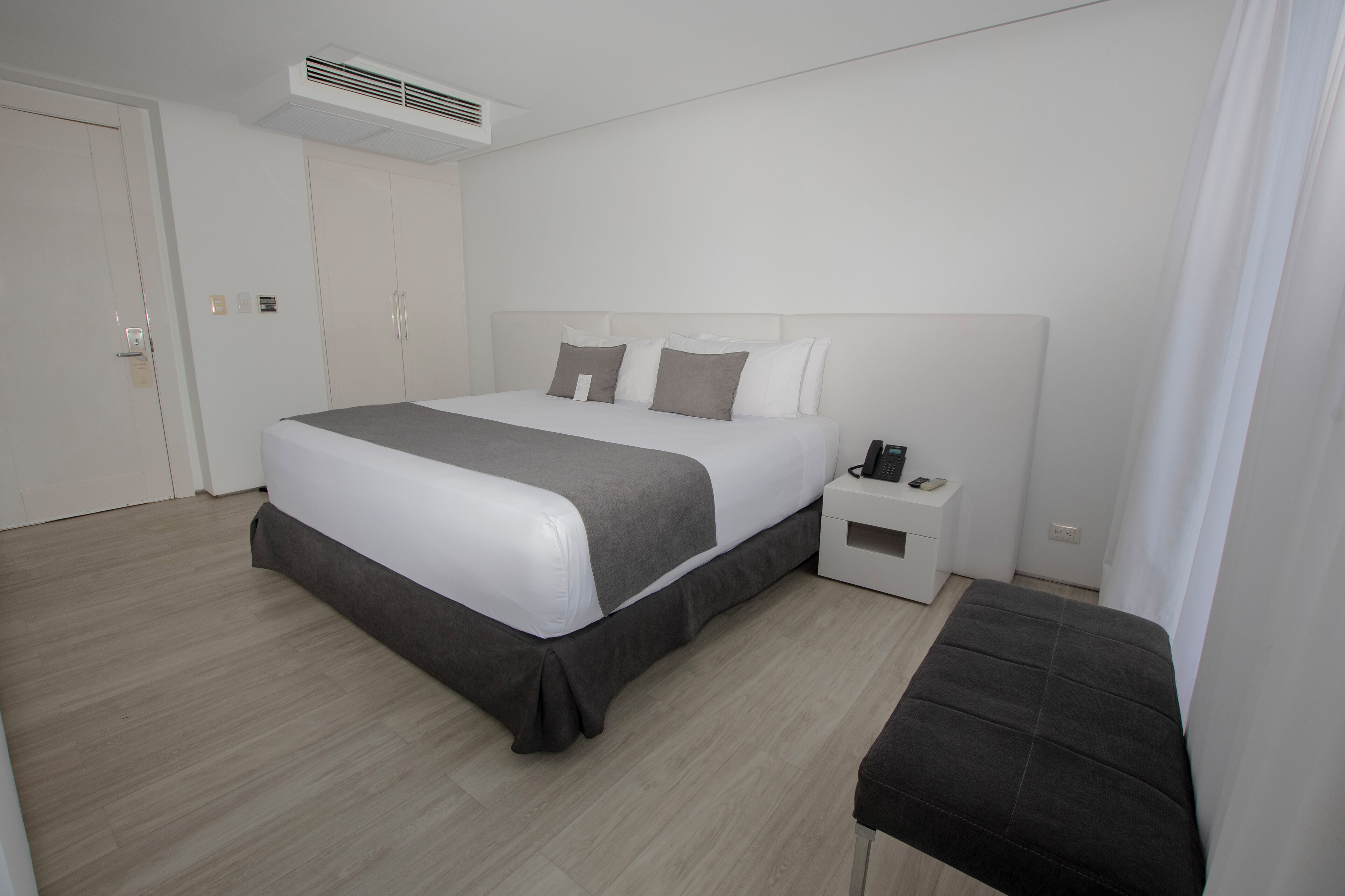 Una habitación de hotel moderna con una cama grande, mesita de noche y un banco.
