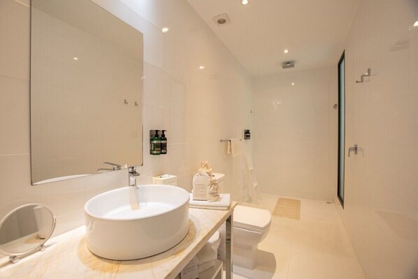 A modern bathroom with a large mirror, a round sink, a toilet, and a shower area. - Golden Bay Galapagos (Puerto Baquerizo Moreno)