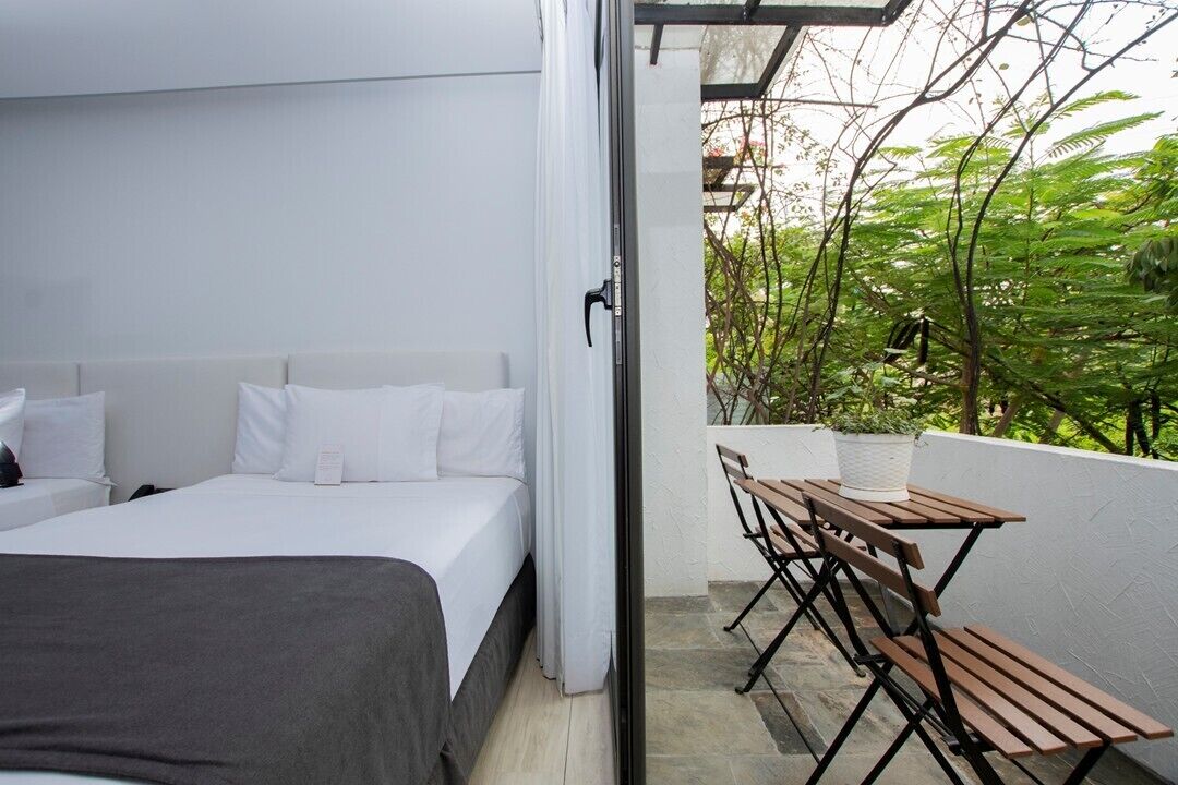A bedroom with a bed, a small table with chairs, and a view of greenery outside.