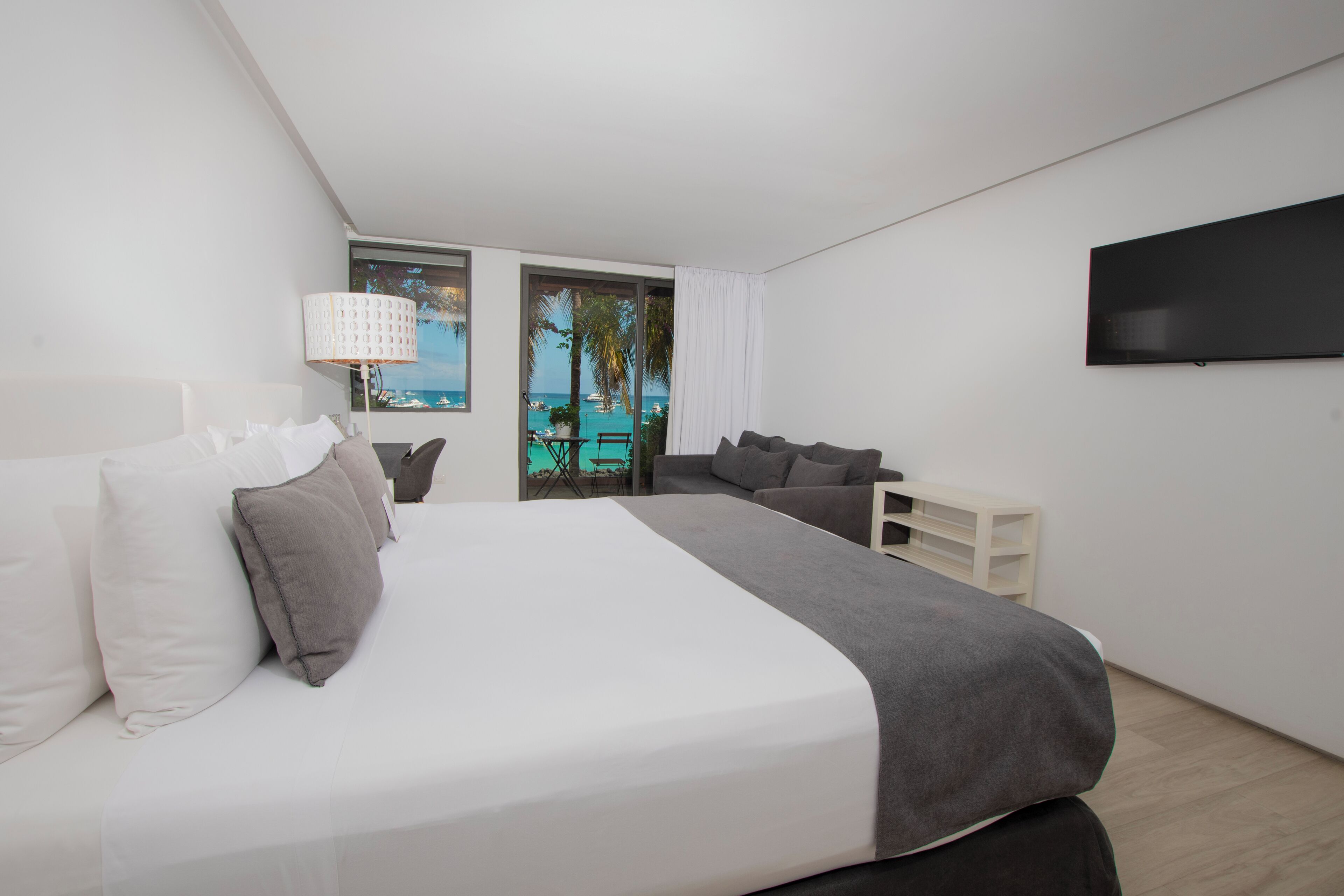 A modern bedroom with a large bed, a TV, and a view of the sea.