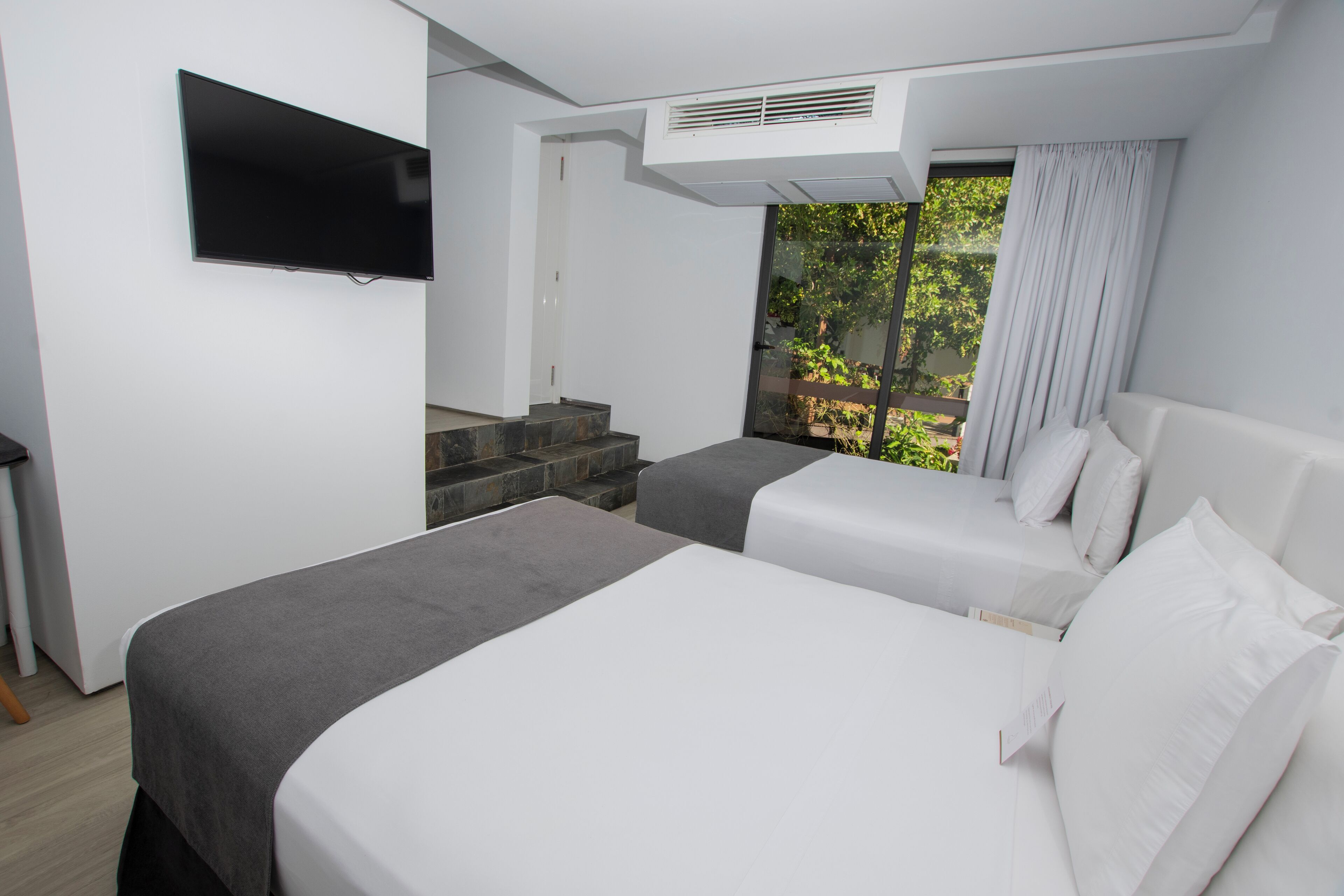 Een moderne hotelkamer met twee bedden, een flatscreen televisie aan de muur, een trap naar een buitenruimte en een groot raam met gordijnen.