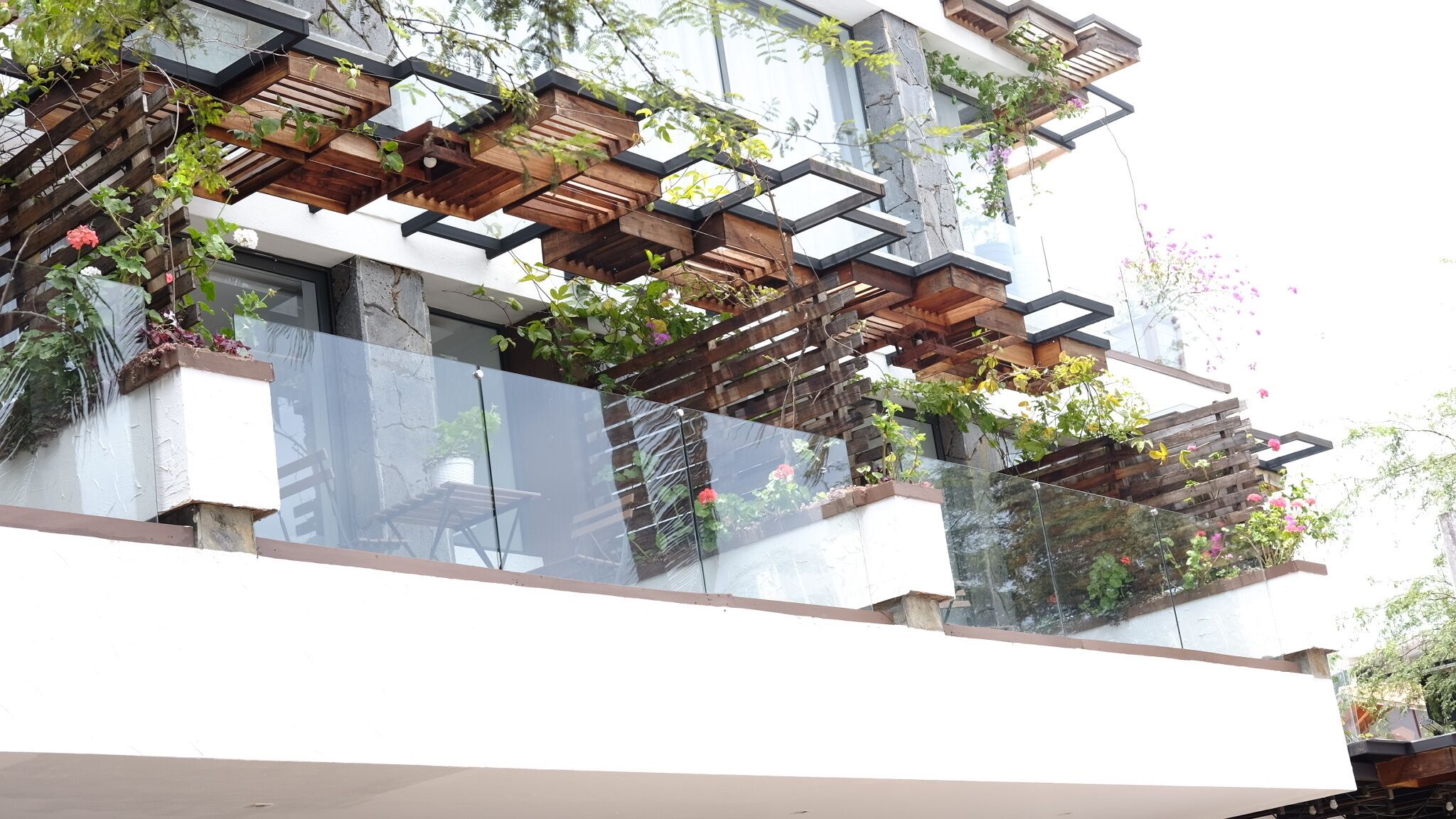 Un edificio moderno con balcón, jardineras de madera y plantas trepadoras.