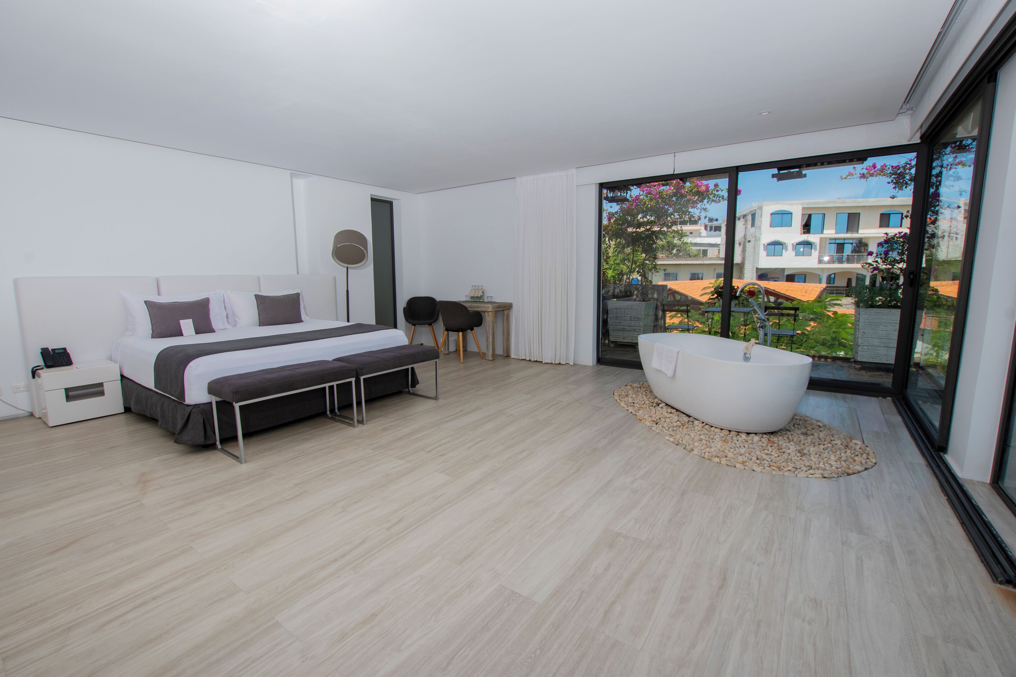 A modern bedroom with a large bed, a bedside table, a chair, a small table, and a bathtub.