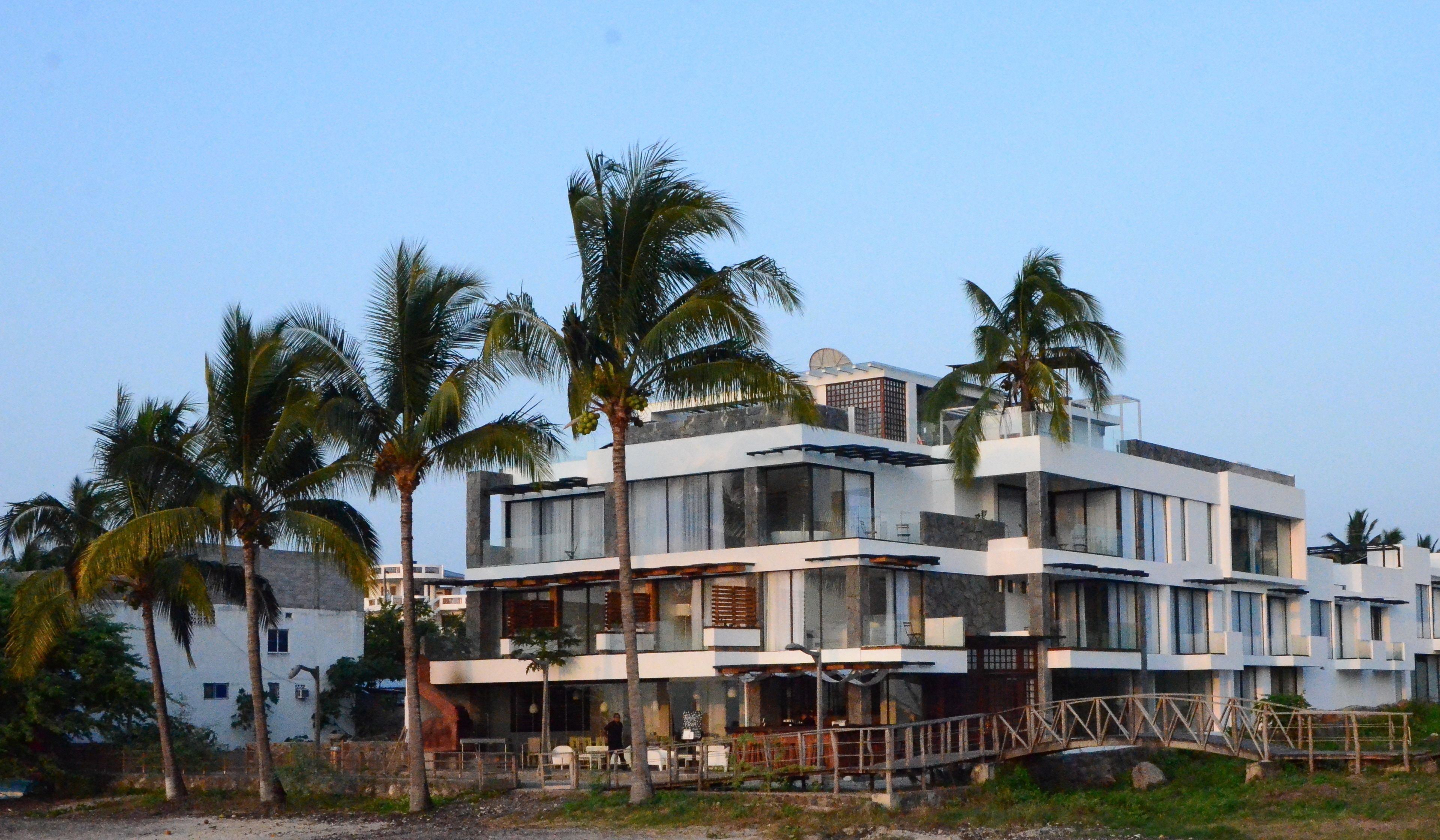 A modern multi-story building with a flat roof, large windows, and a covered outdoor seating area.