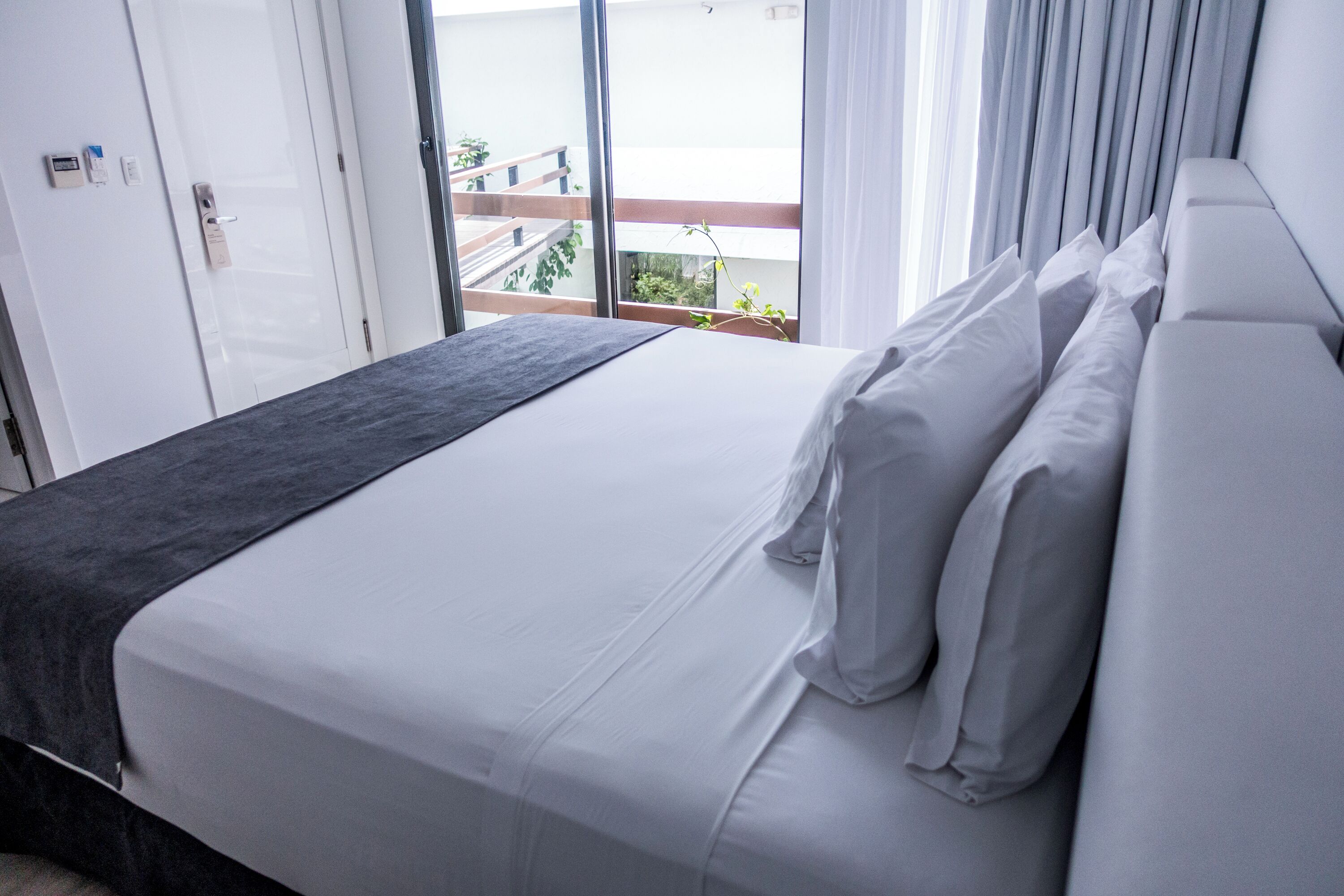 A modern hotel room with a large bed, a view of the balcony, and a door with a handle.