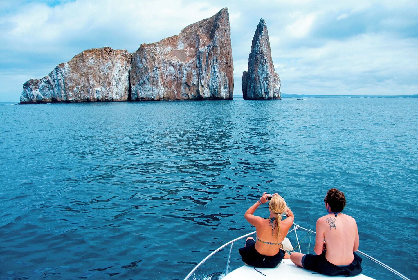 Two people on a boat with a large rock formation in the background.
