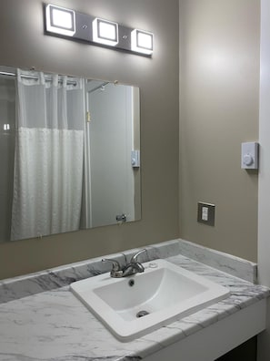 A bathroom with a white sink, a mirror, and a shower curtain. - Imperial Motel (100 Mile House)