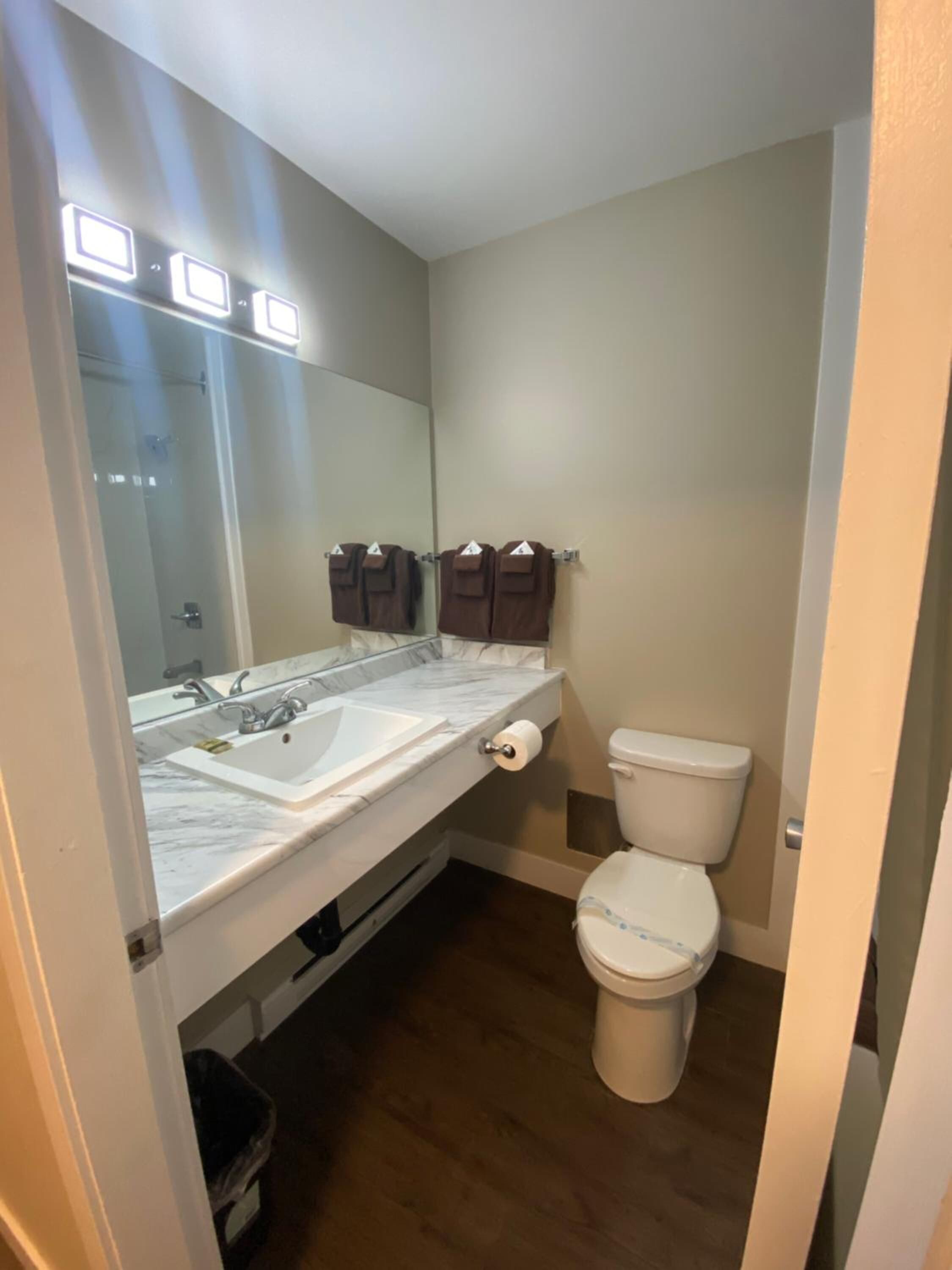 A bathroom with a white sink, mirror, and toilet. There are brown towels hanging on hooks.