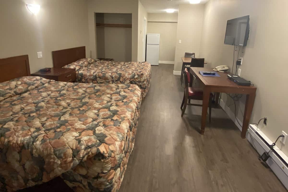 Ein Zimmer mit zwei Betten, einem Schreibtisch, einem Stuhl, einem Kühlschrank und einem an der Wand montierten Fernseher.