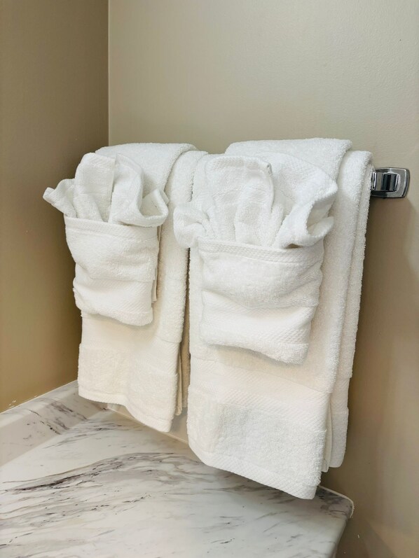 Un baño con dos toallas blancas colgadas en un toallero metálico, un lavabo de mármol y una pared color beige.