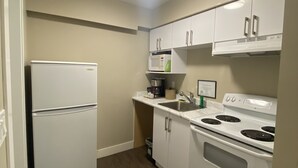 A compact kitchen with white appliances, a built-in microwave, and a stove. - Imperial Motel (100 Mile House)