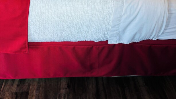A hotel room with two beds, each with red and white bedding, and a wooden nightstand between them. - Imperial Motel (100 Mile House)